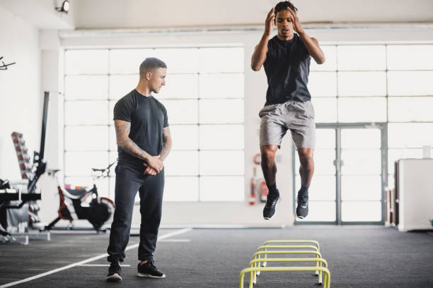 Athlete having a personal training session in the gym. He is doing warm up exercises while his personal trainer guides him.
